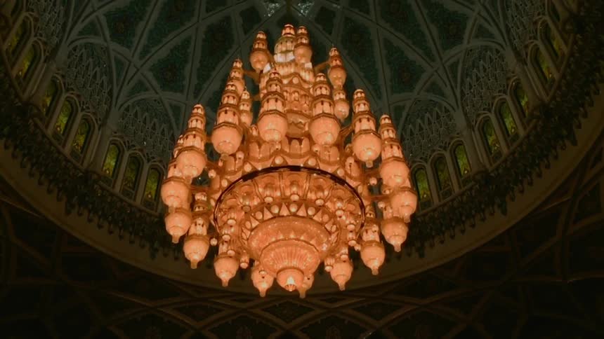 An enormous and elaborate chandelier hangs from the ceiling of the interior of a dome with phenomenal architecture