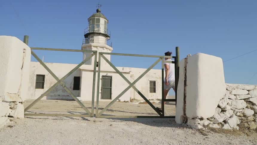 A man jumps a small fence to access a lighthouse