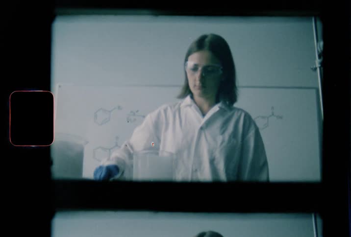 A female lab technician drops a cube into a beaker filled with liquid