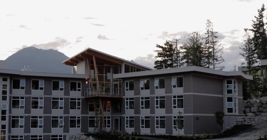 A hotel with stone walls built on a high elevation with trees above and mountains on the horizon