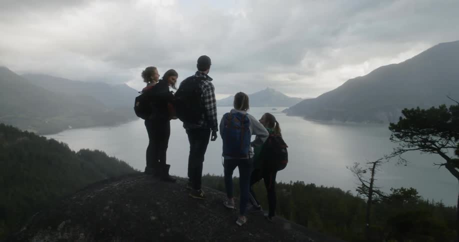 Friends stand on hill looking over lake and mountains