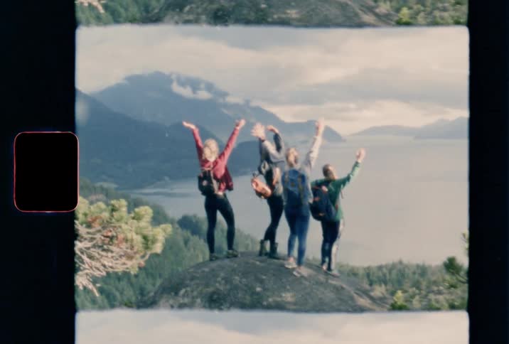 A group of young women standing on a boulder and cheering while looking out over a lake