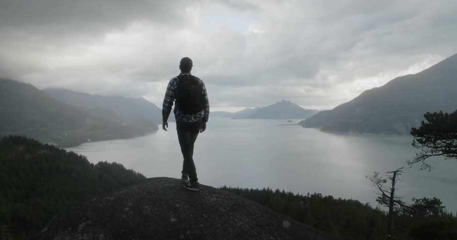 Man hikes onto stone hill overlooking lake and mountains