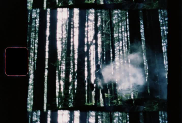 Film footage of a person standing in a dark forest with smoke around him