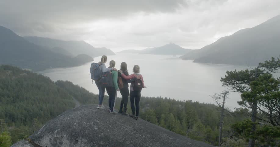 A group of young woman standing on a boulder at high altitude looking at the forest and river far below