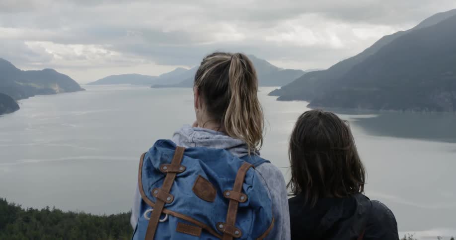 Two girls standing on a cliff overlooking a lake and mountains