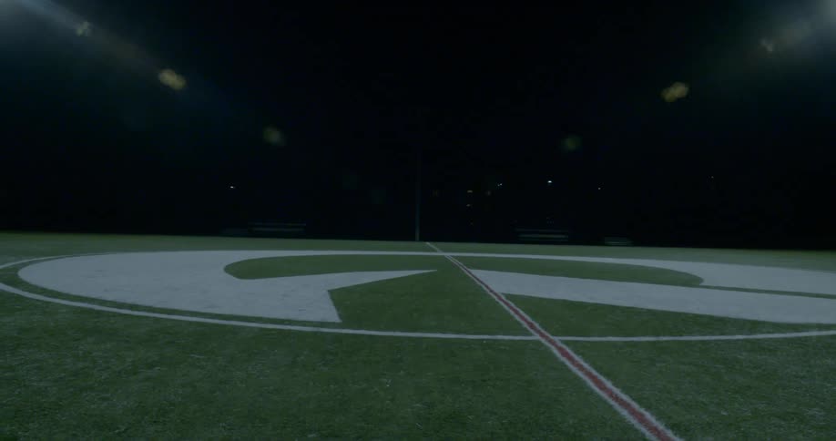 A logo painted on the grass midfield of an empty athletic field with lights shining down