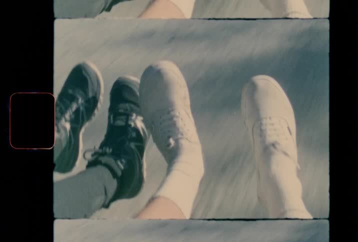 Two people playfully dangle their feet over a dirt road as they are being transported in a vehicle