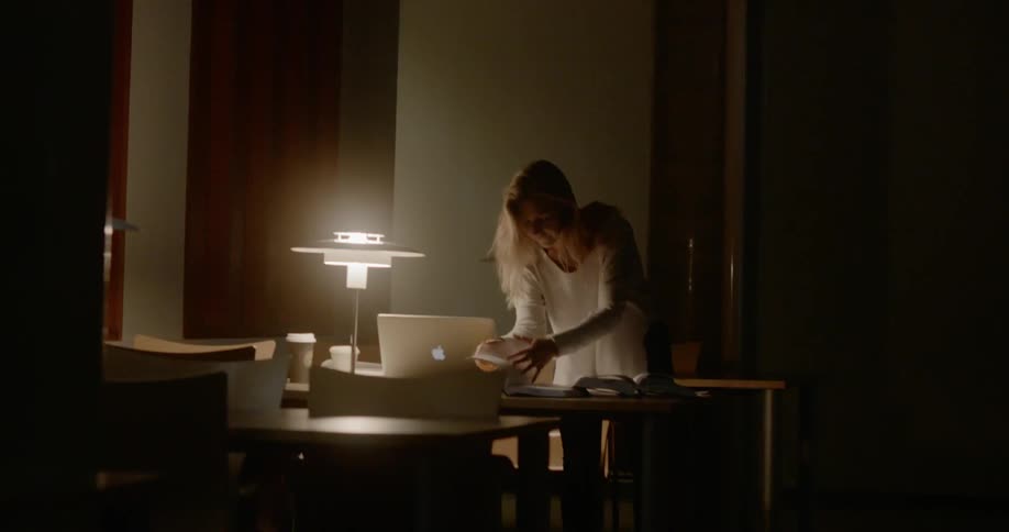 A blonde woman leafs through a book on her desk