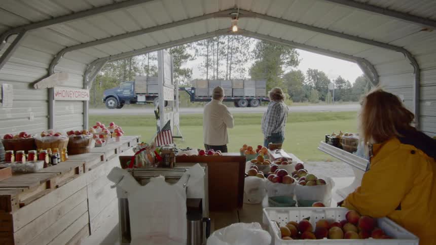 People at a fruit stand watch a truck drive by