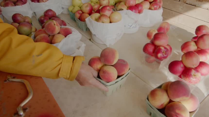 A person sets peaches out in a basket at a fruit stand
