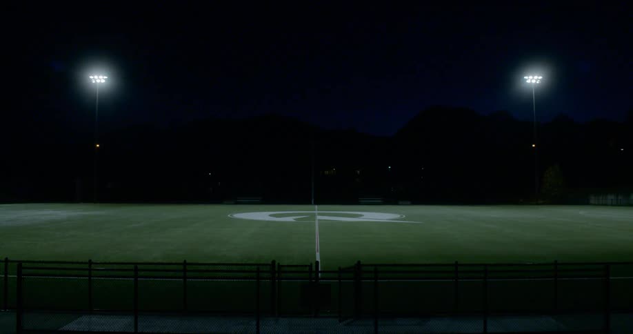 Lights shine down on the grass of an empty athletic field at night