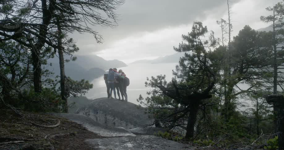 A group of girls run to the top of a rock and hug