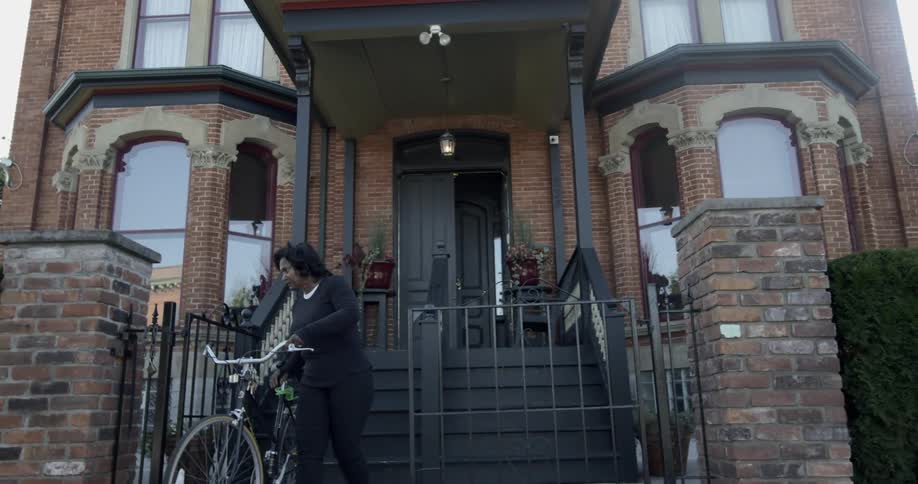 A woman lifts a bicycle down the front steps of a home to the sidewalk