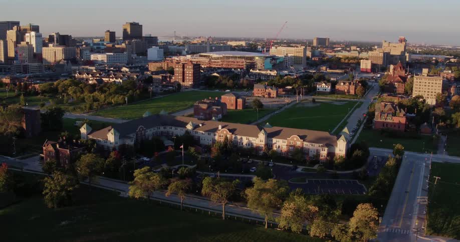 Passing over the grounds fields roads and parking lot of a campus with a city skyline behind