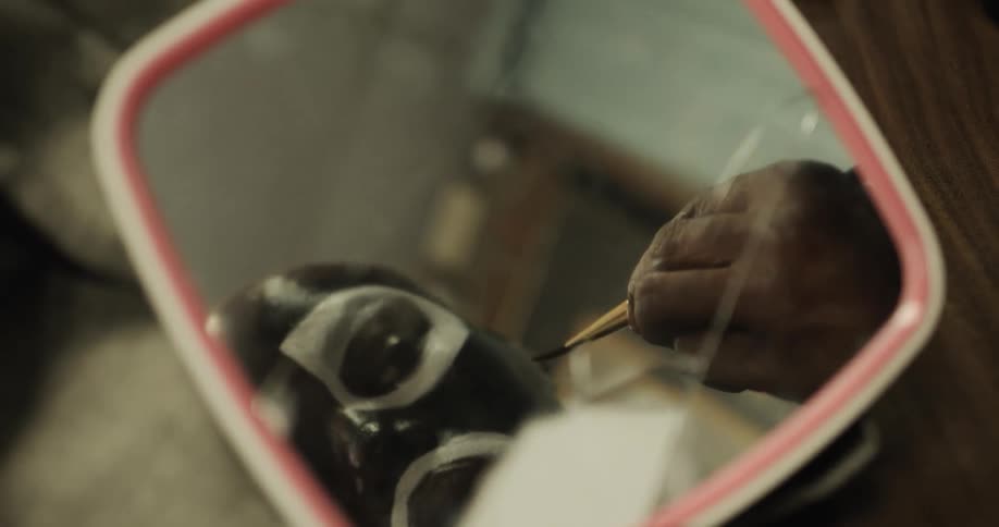 Black man looks in a mirror as he paints his face
