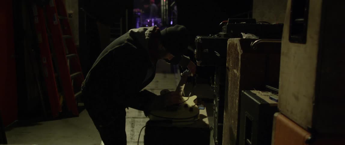 A man leans over an electric guitar as he works to adjust its strings backstage