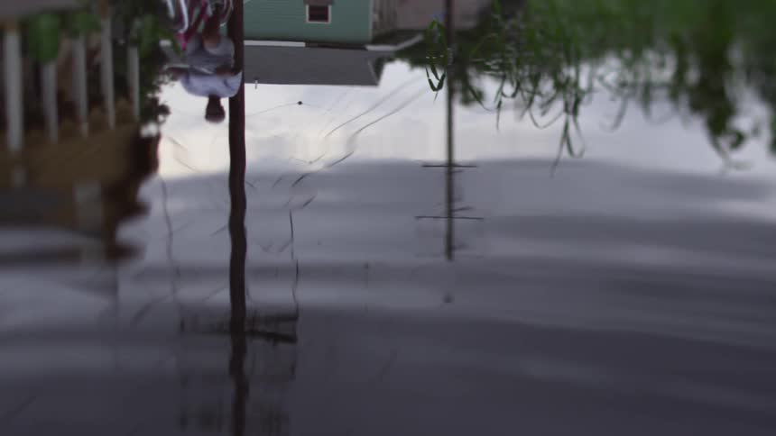 A puddle reflects buildings as a person bicycles by