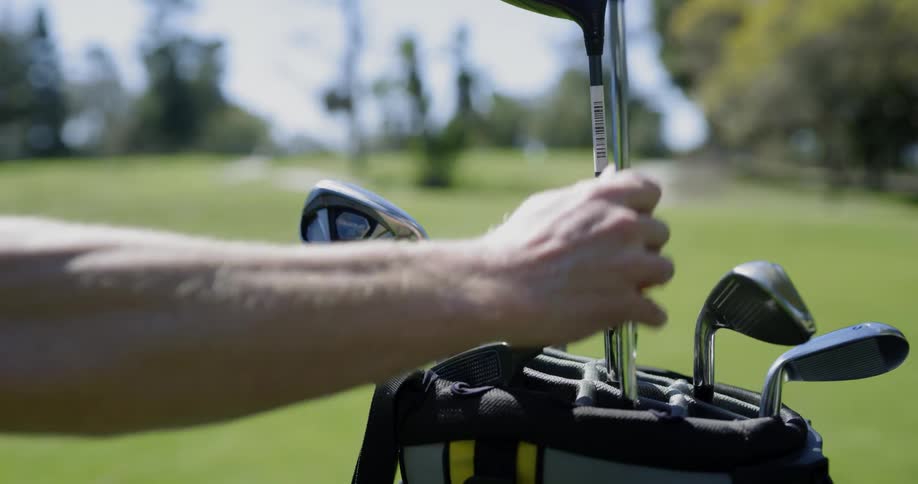 A mans arm taking a golf club out of a bag with the golf course in the background
