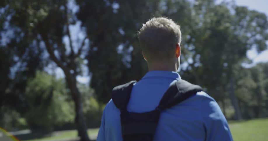 A man walking in a field with a harness attached to his back