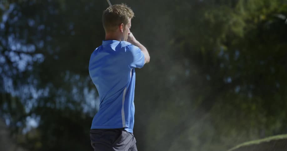 A golfer hitting a golf ball from a sand bank