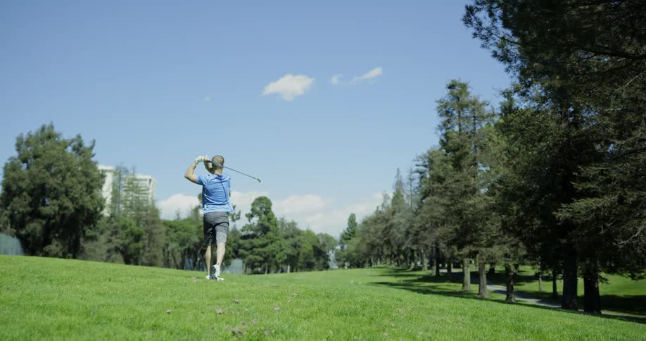 A man standing on a grassy golf course swings his golf club and strikes a ball off into the distance
