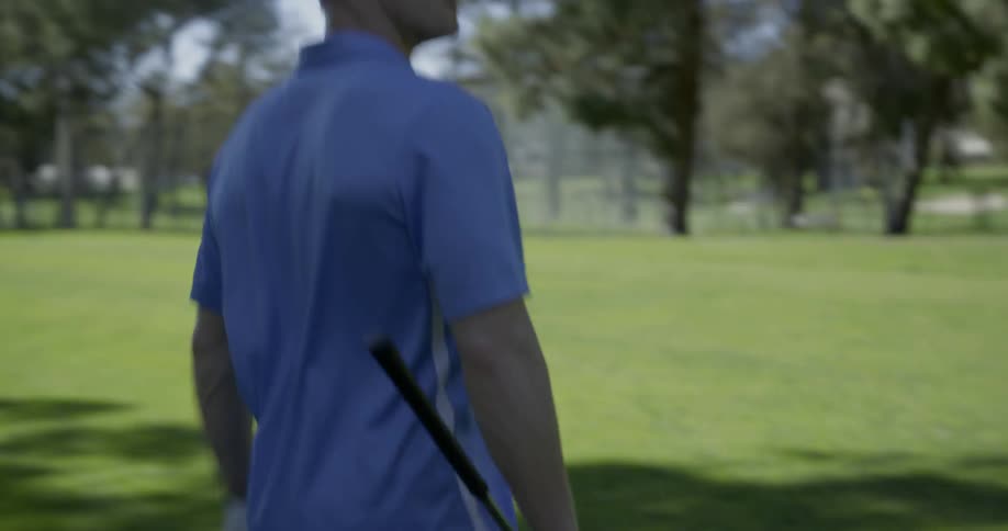A man carrying a club walks across the green on a sunny day