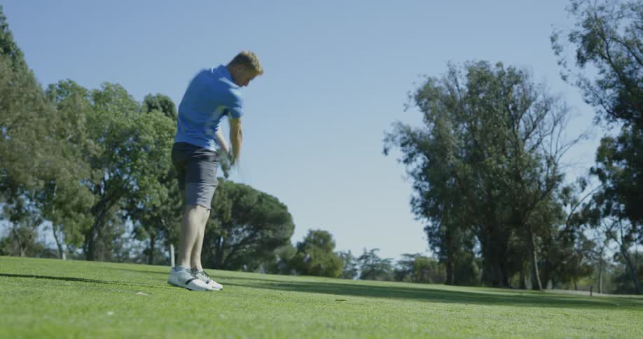 Male golfer hitting ball and walking after it at a golf course