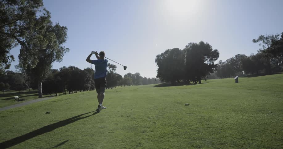 Man tees off on golf green under clear blue sky