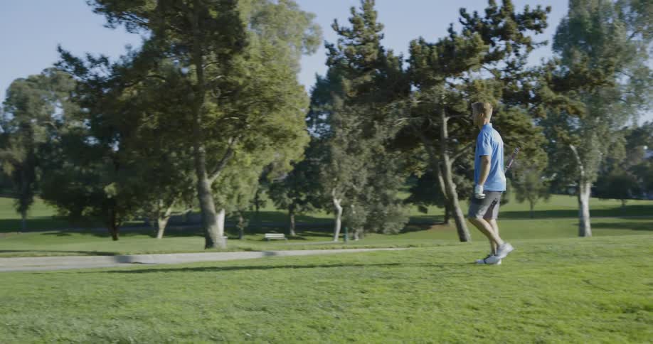A white male in a blue polo shirt is walking into a sand bunker on a golf course