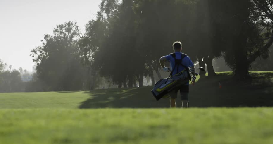 A man is carrying his golf bag across the course