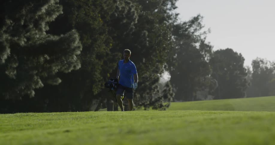 A golfer carries his clubs across the field
