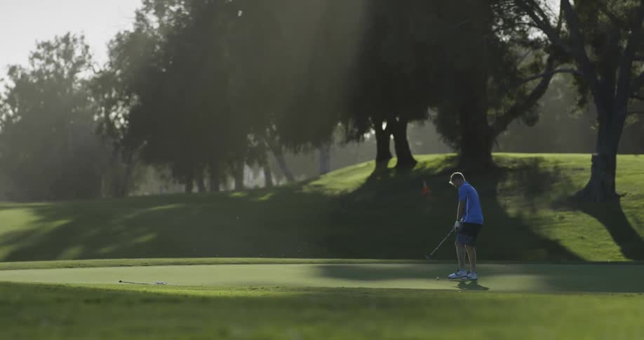 Golf player uses a club to hit the ball into the hole on a course