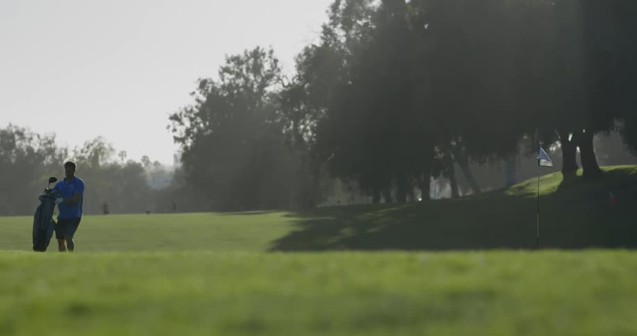 Golfer takes club out of bag and walks to the flag