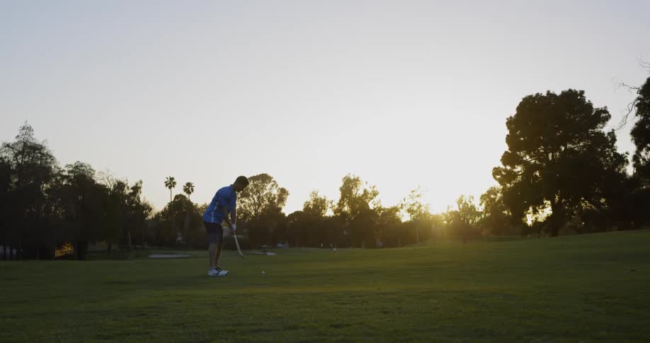 A golfer hits the ball from the green at sunset