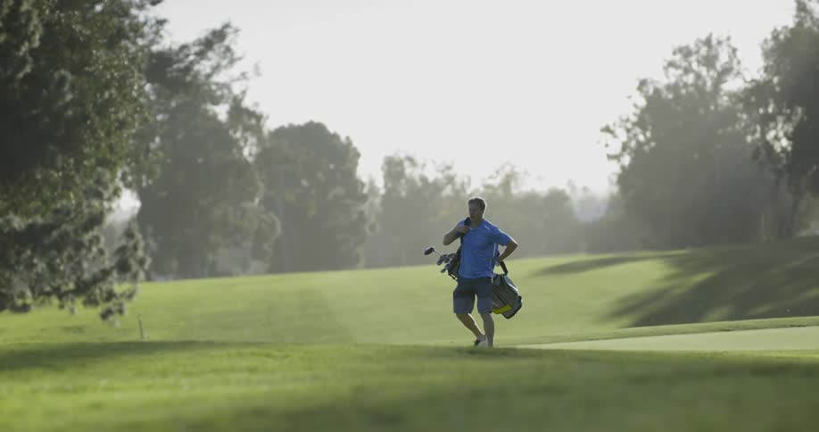 A man on a golfing green putting the straps of his golfing bag over his shoulder before walking off