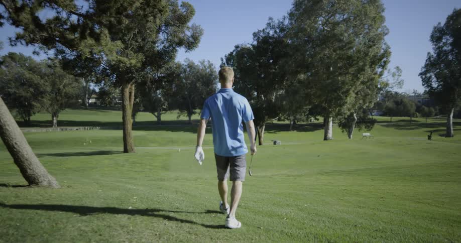 Golf player holding club walks on the grass on a sunny day