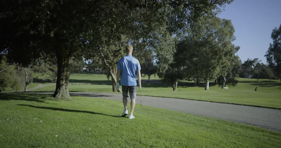 Golf player holding a club walks on the grass on a course