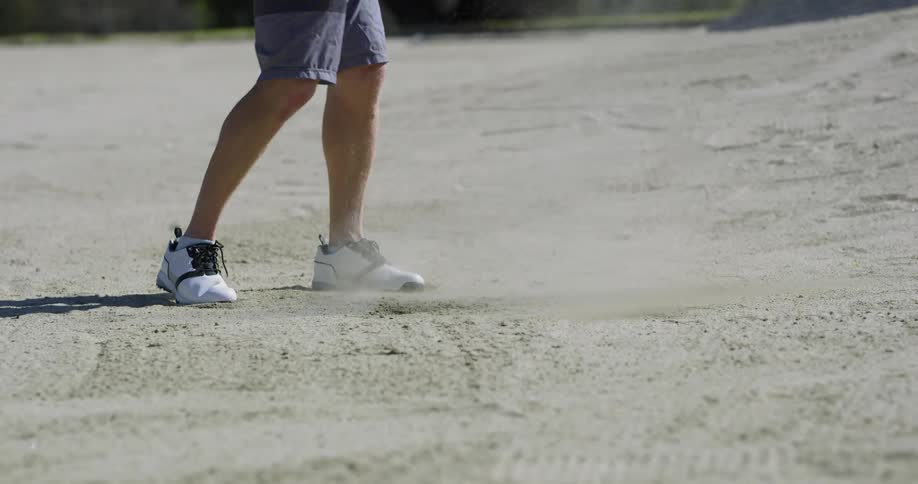 Male swings a golf club and hits a golf ball out of a sand pit on the golf course