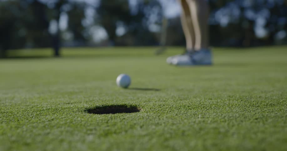 Golf player uses a club to hit the ball into the hole on a course