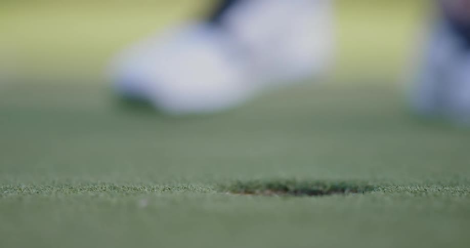A golfer putts a golf ball into the hole