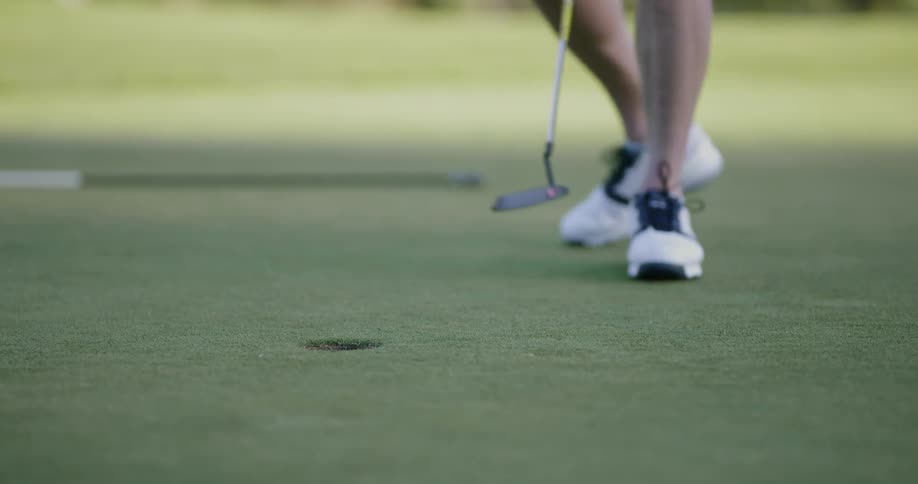 A golfer sinks a putt then reaches into the hole and removes the ball