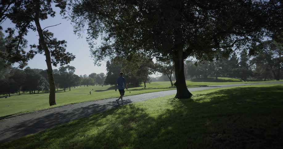 A man carries a golf club and walks along a path