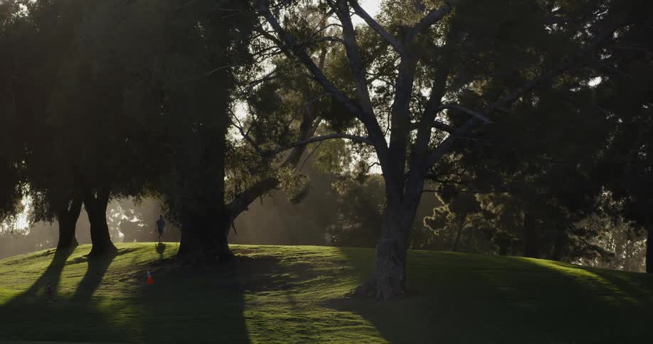 Golf player walks on the green grass in the far distance at sunset