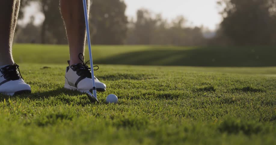 A man with a golf club steps forward to the golf ball and hits it