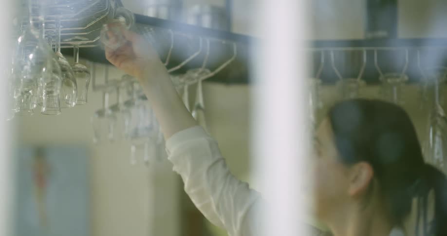 A woman removes a wine glass from an overhead rack