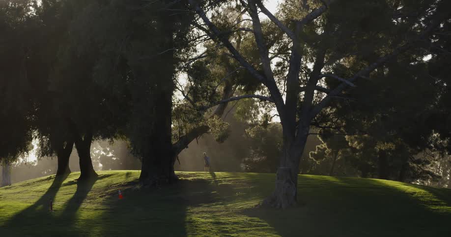 Man prepares and swings golf club on hill near trees