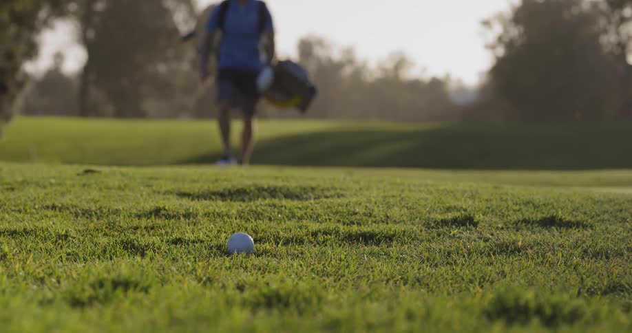 A man is walking towards the golf ball