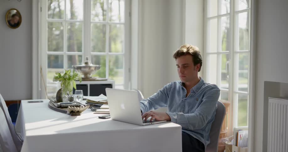 A man sits at a table and types on a laptop