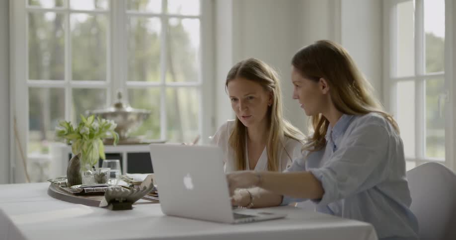 A woman types on a laptop and then shows the screen to another woman